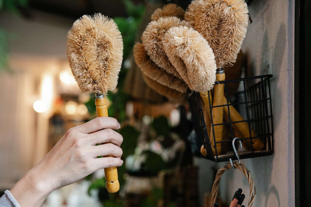 Close-up of a hand selecting eco-friendly cleaning brushes from a basket indoors.